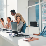 Team of customer support or IT professionals wearing headsets, collaborating at desks with laptops in a modern office.