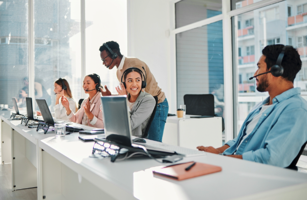 Team of customer support or IT professionals wearing headsets, collaborating at desks with laptops in a modern office.