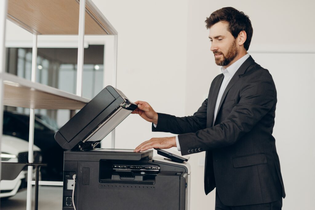Business professional using a multifunction office printer to scan documents in a modern workplace, demonstrating managed print services for businesses.